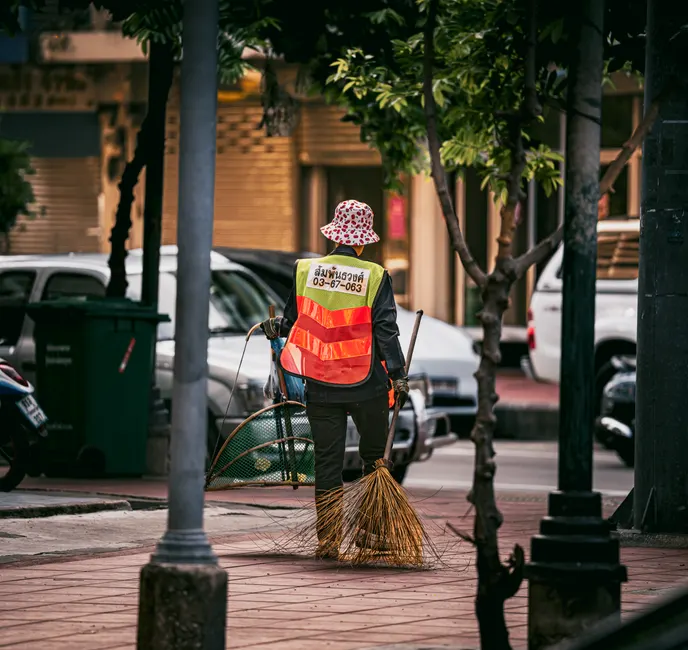A street cleaner in Bangkok cleans sidewalks with tools, showcasing urban life.